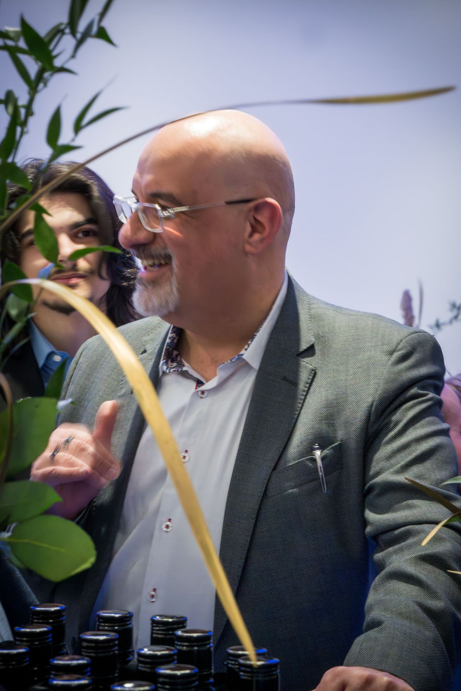 A person in a gray suit jacket sips a drink at a social gathering.