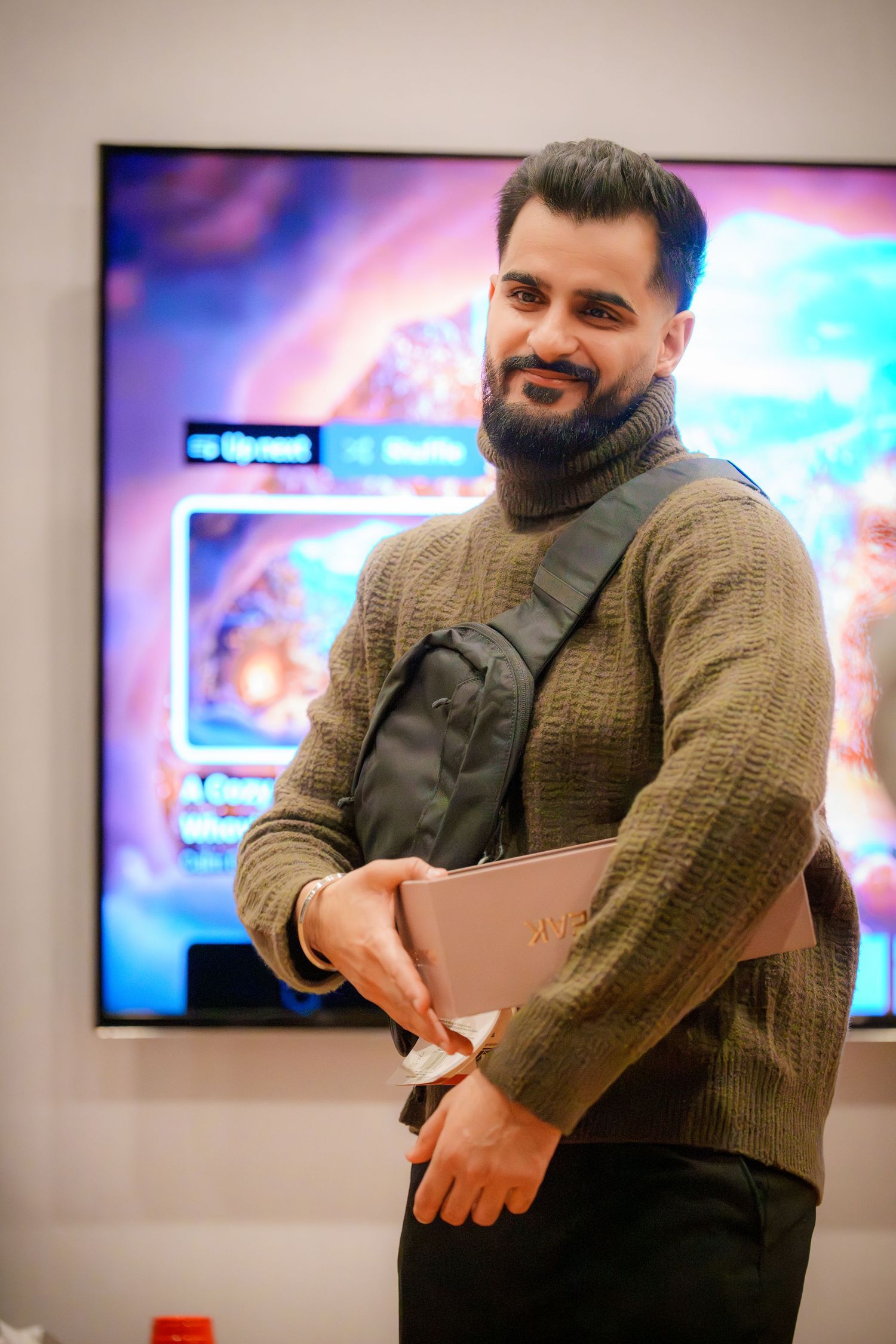 Person in knit sweater smiles while engaging with others at indoor event.