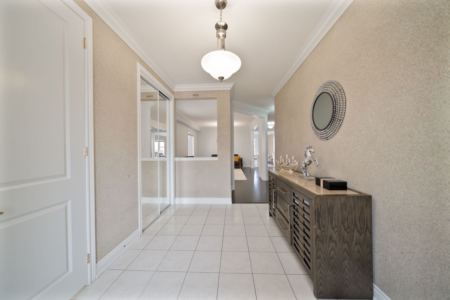 Long white hallway with pendant lighting fixtures and gray tile flooring leads to a bright window at the end.