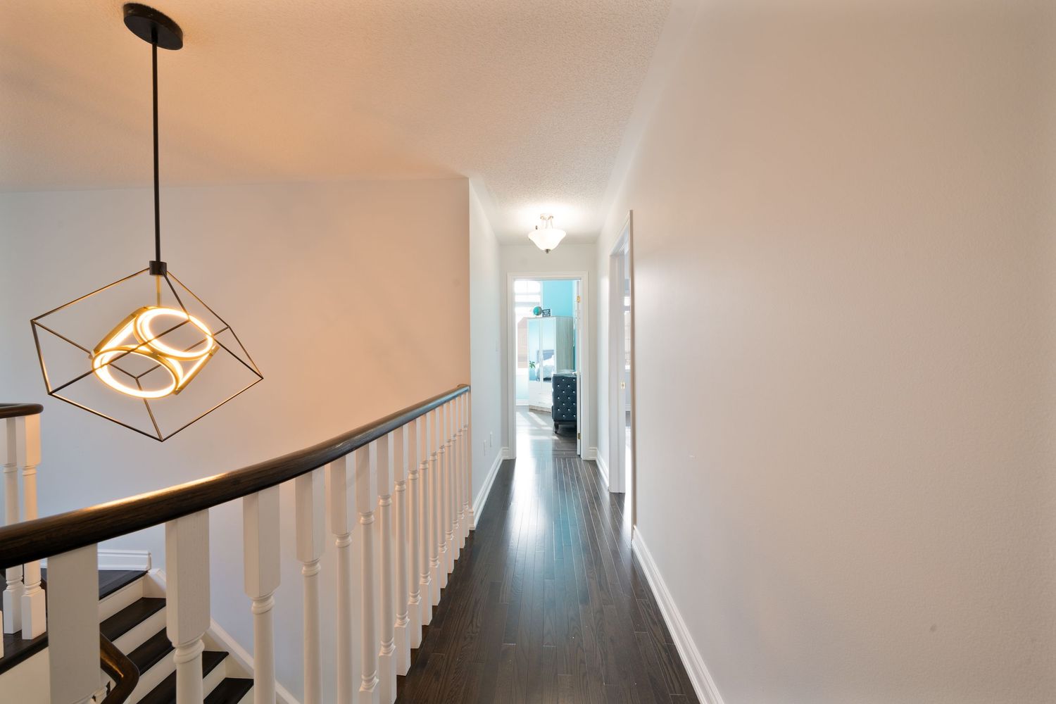 Modern white hallway with geometric pendant light fixtures and black handrails along the staircase.