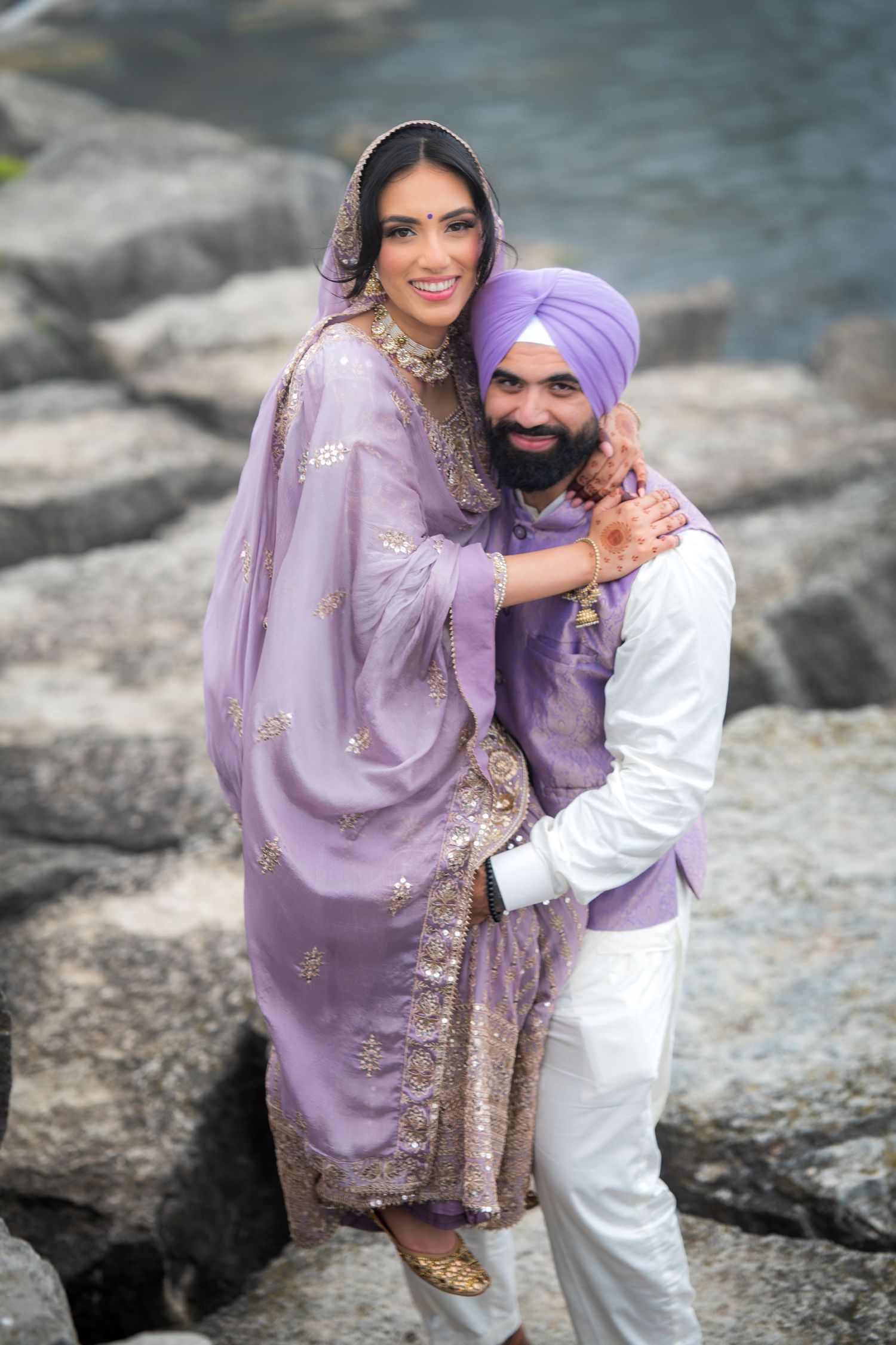 Couple in matching purple and white traditional clothing share intimate moments by water.