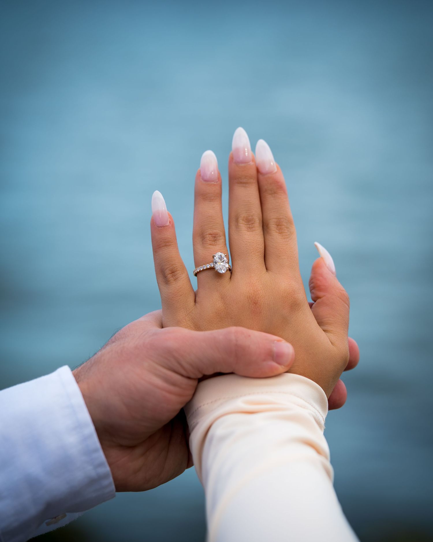 Close-up of hands with engagement ring against ocean backdrop showing intimate connection.