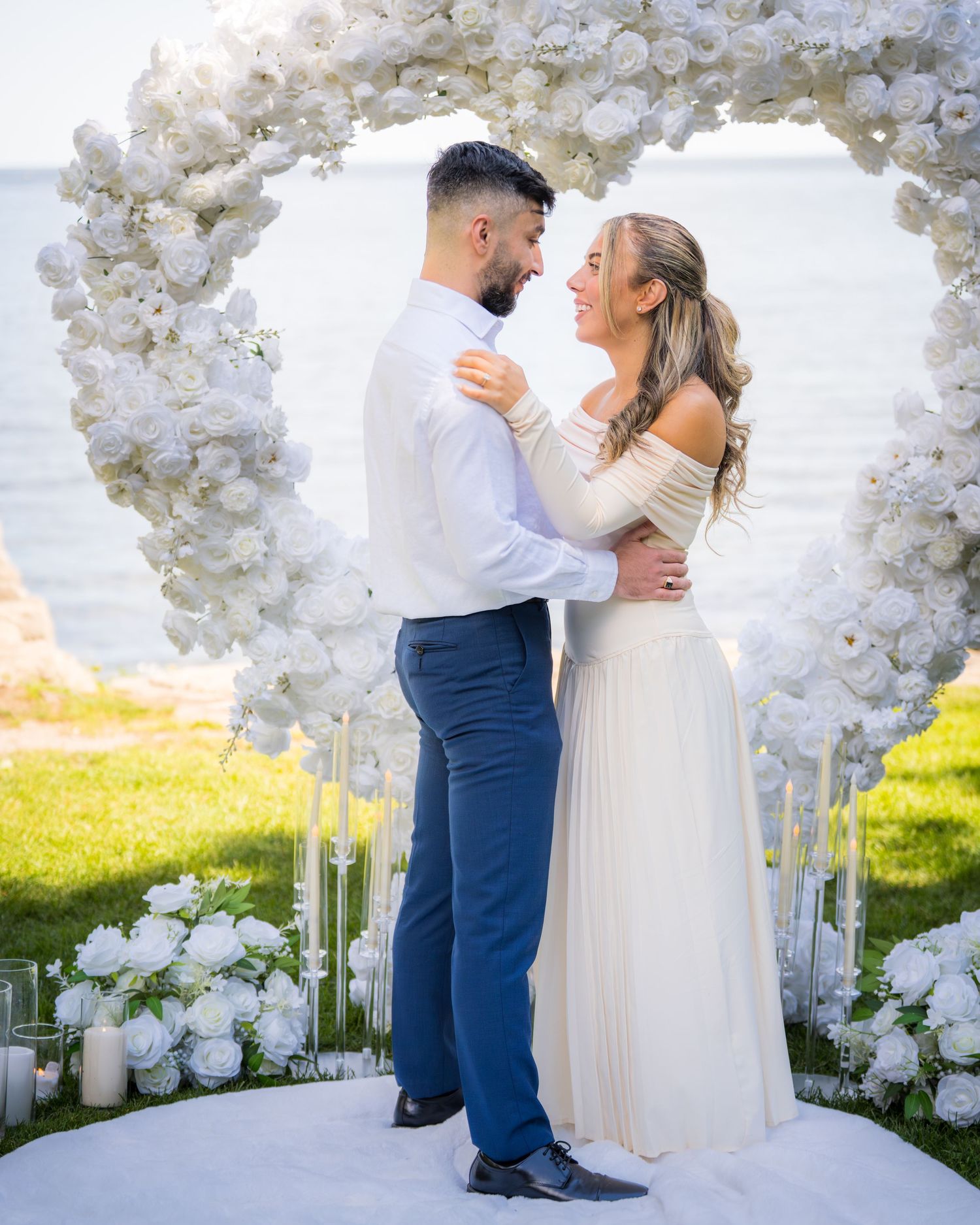Wedding ceremony site with white floral arch and scattered petals creating romantic atmosphere by the sea.