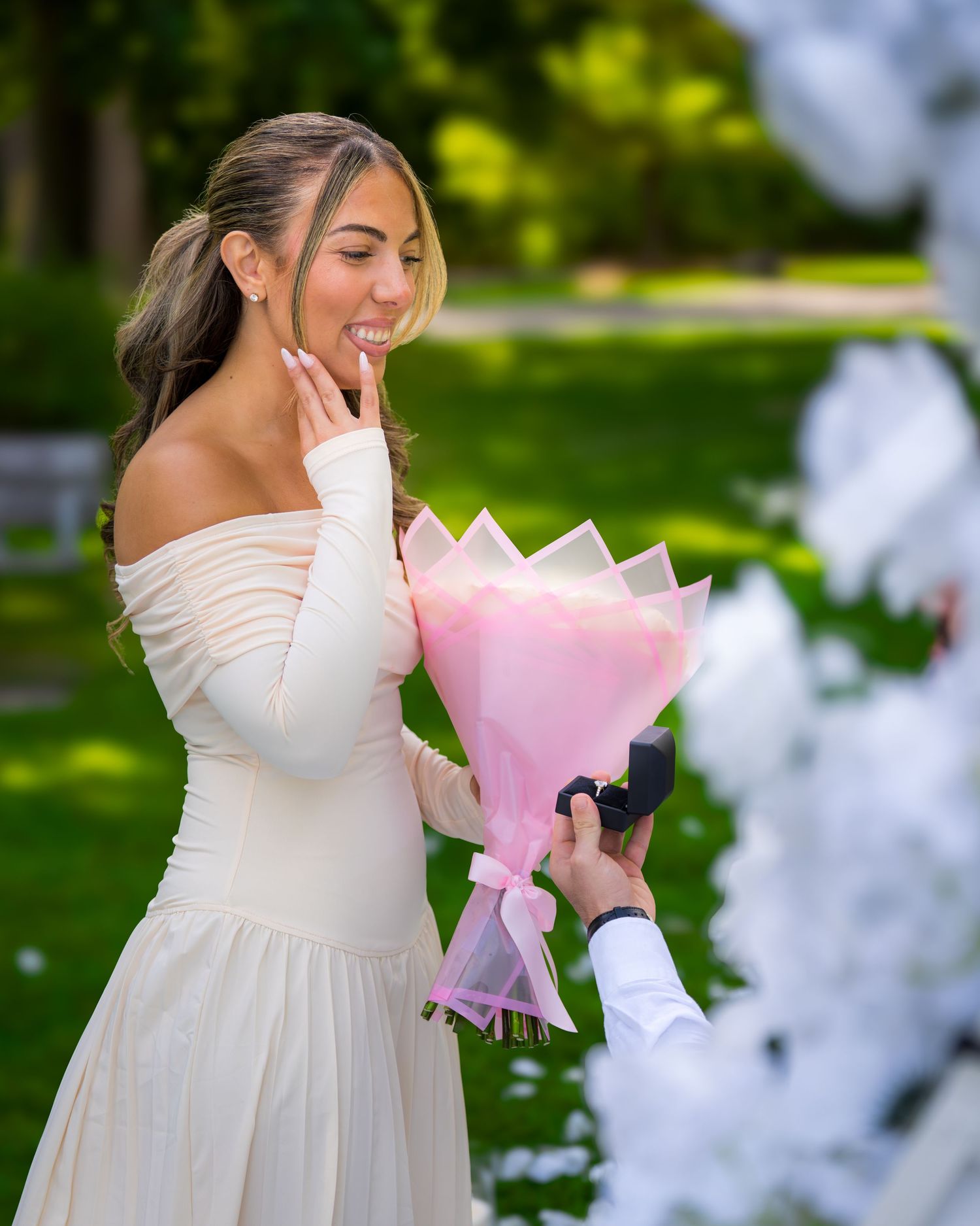 A joyful reaction captured during a garden proposal with pink flowers and white decorations.