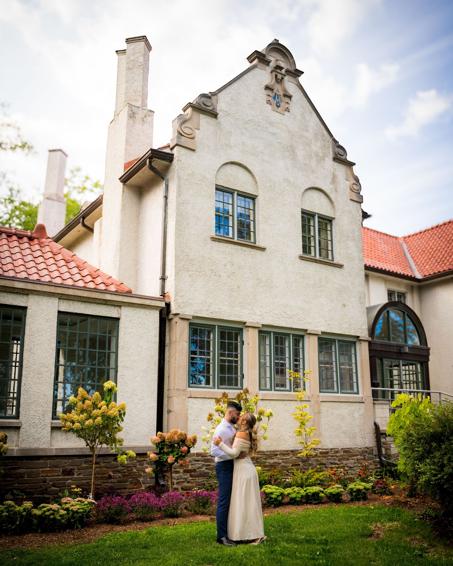 Elegant white stucco building with Tudor-style architecture features green-trimmed windows and red tile roof.