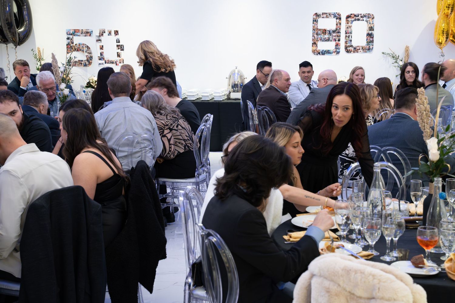 Corporate event attendees socializing around tables with wine glasses and decorative elements.