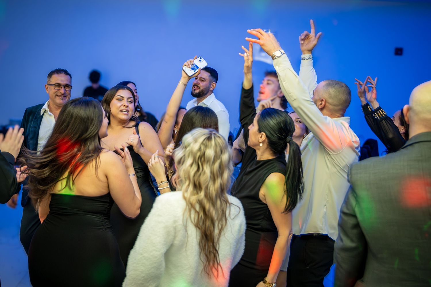 People dancing with raised arms under blue event lighting at a celebration.