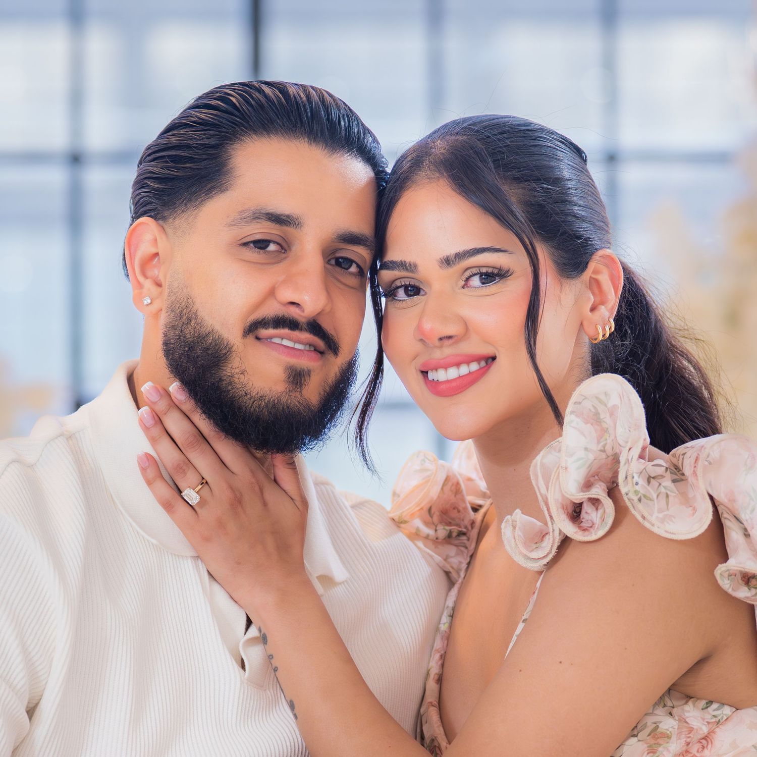 Smiling couple posing closely together in a bright floral setting during a romantic engagement photoshoot.