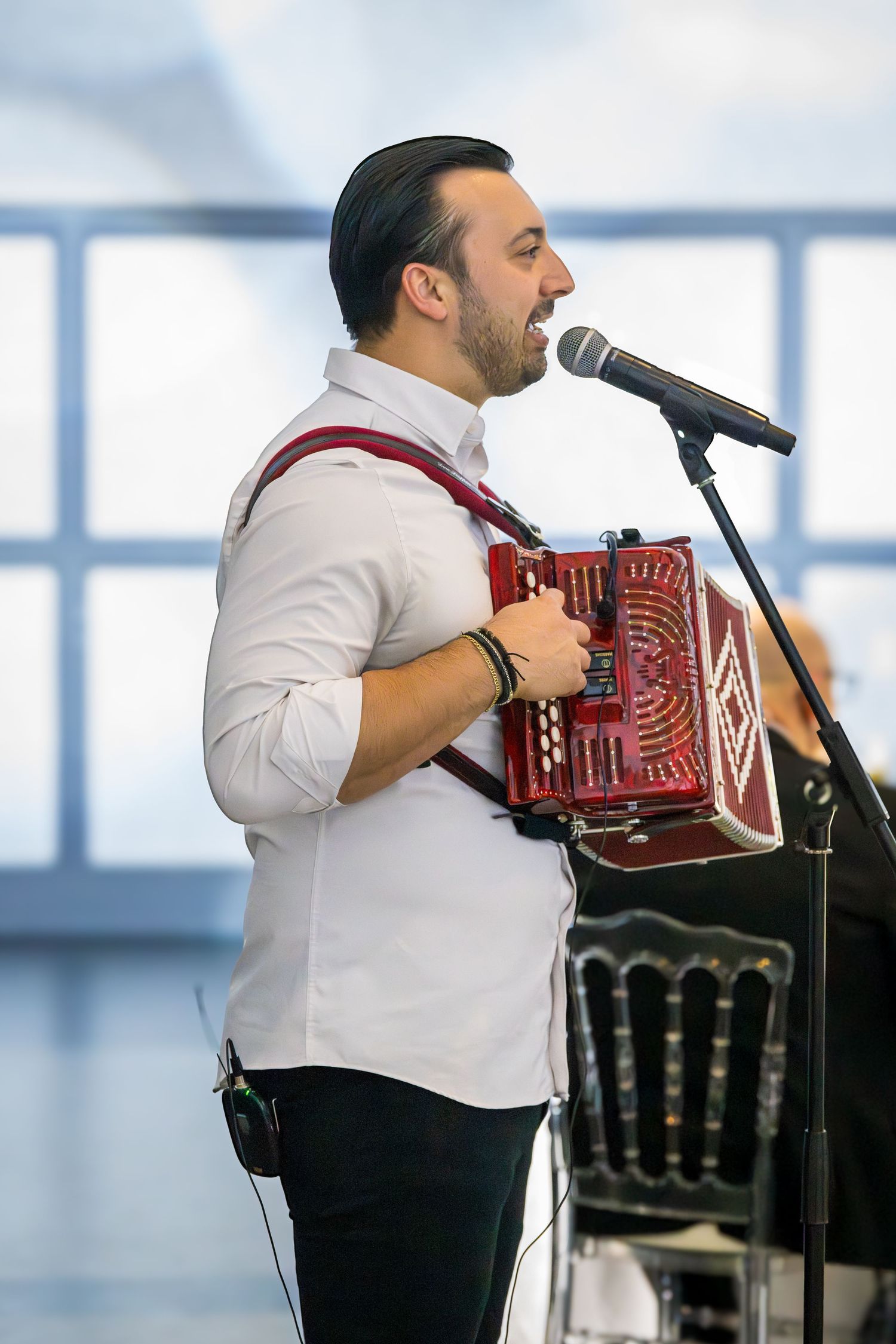 Male accordion player in white shirt performing and singing into a microphone at a celebration event.