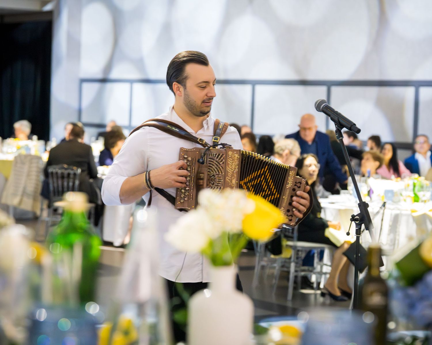 Musician playing accordion at elegant wedding reception with guests dining in background.
