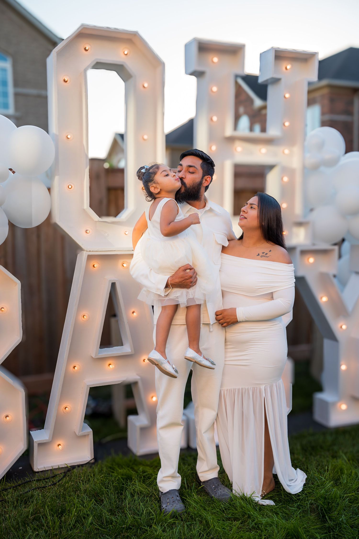 Family in white outfits at an OH BABY gender reveal party with marquee letters and white balloons.