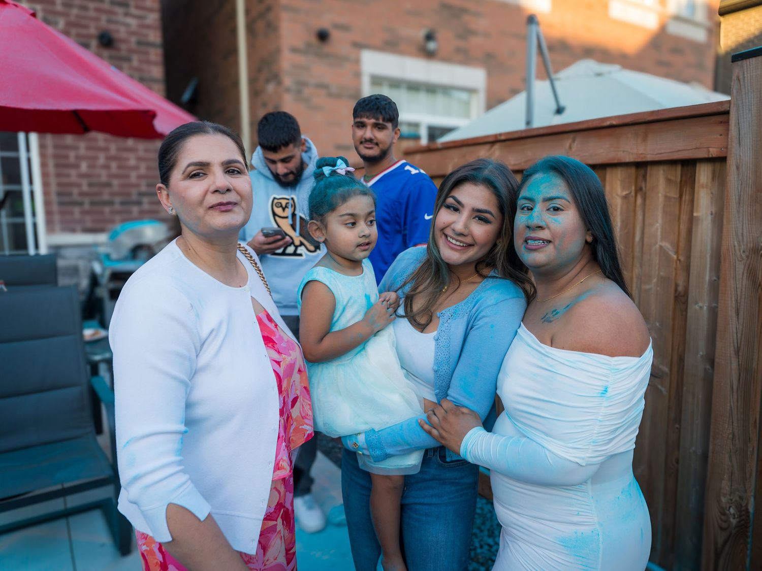 Group of women and children smiling together covered in blue powder at a gender reveal celebration.