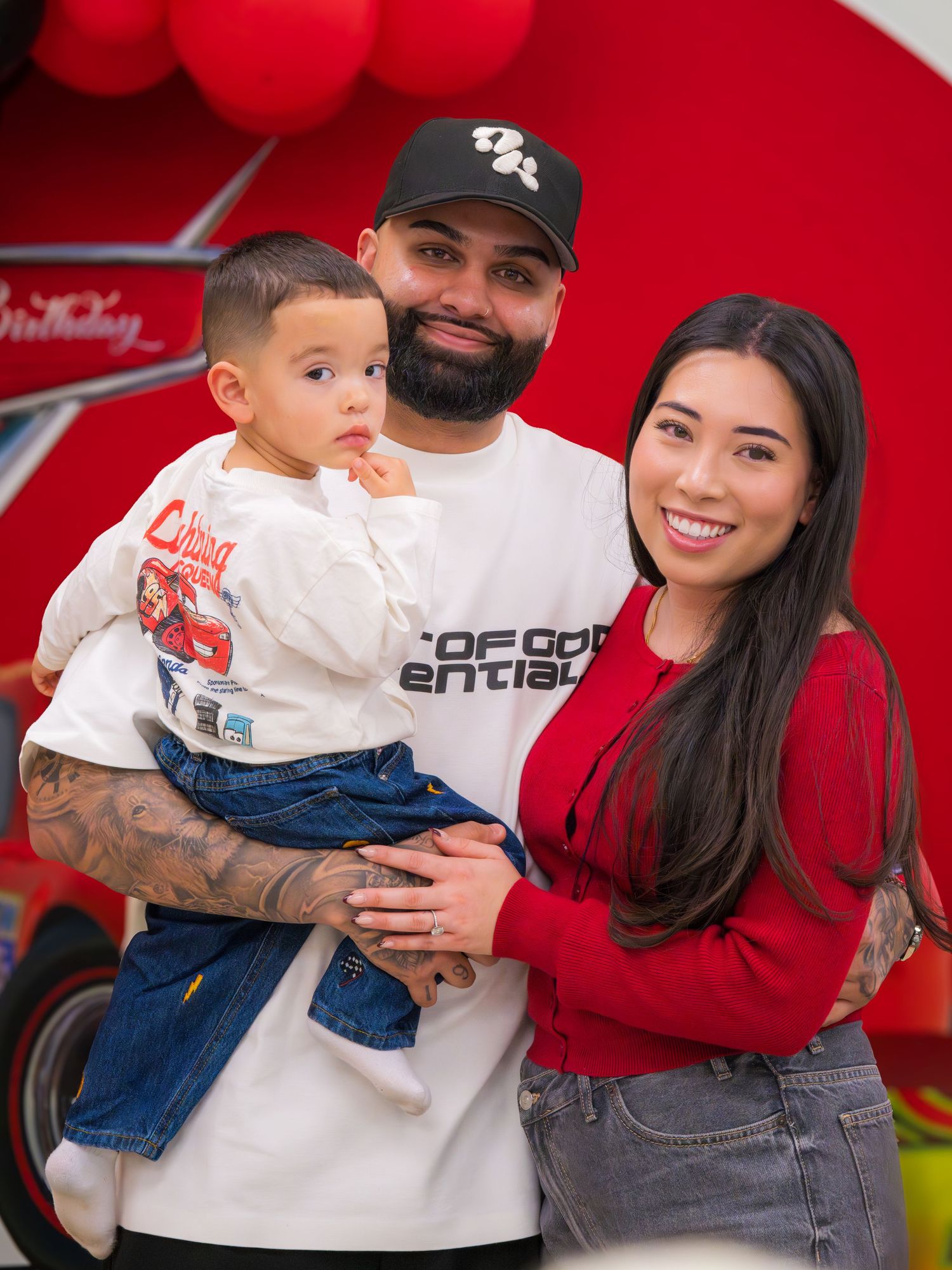 Smiling family posing together at a Cars-themed birthday party with red balloons in the background.