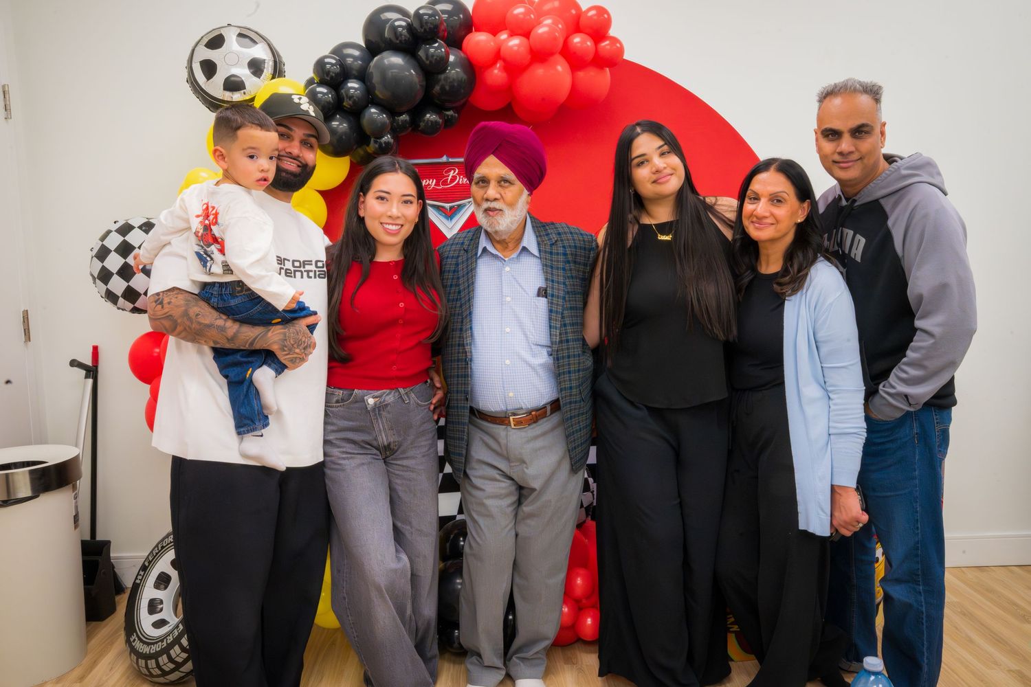 Family group photo at a Cars-themed birthday party with red balloon arch backdrop.