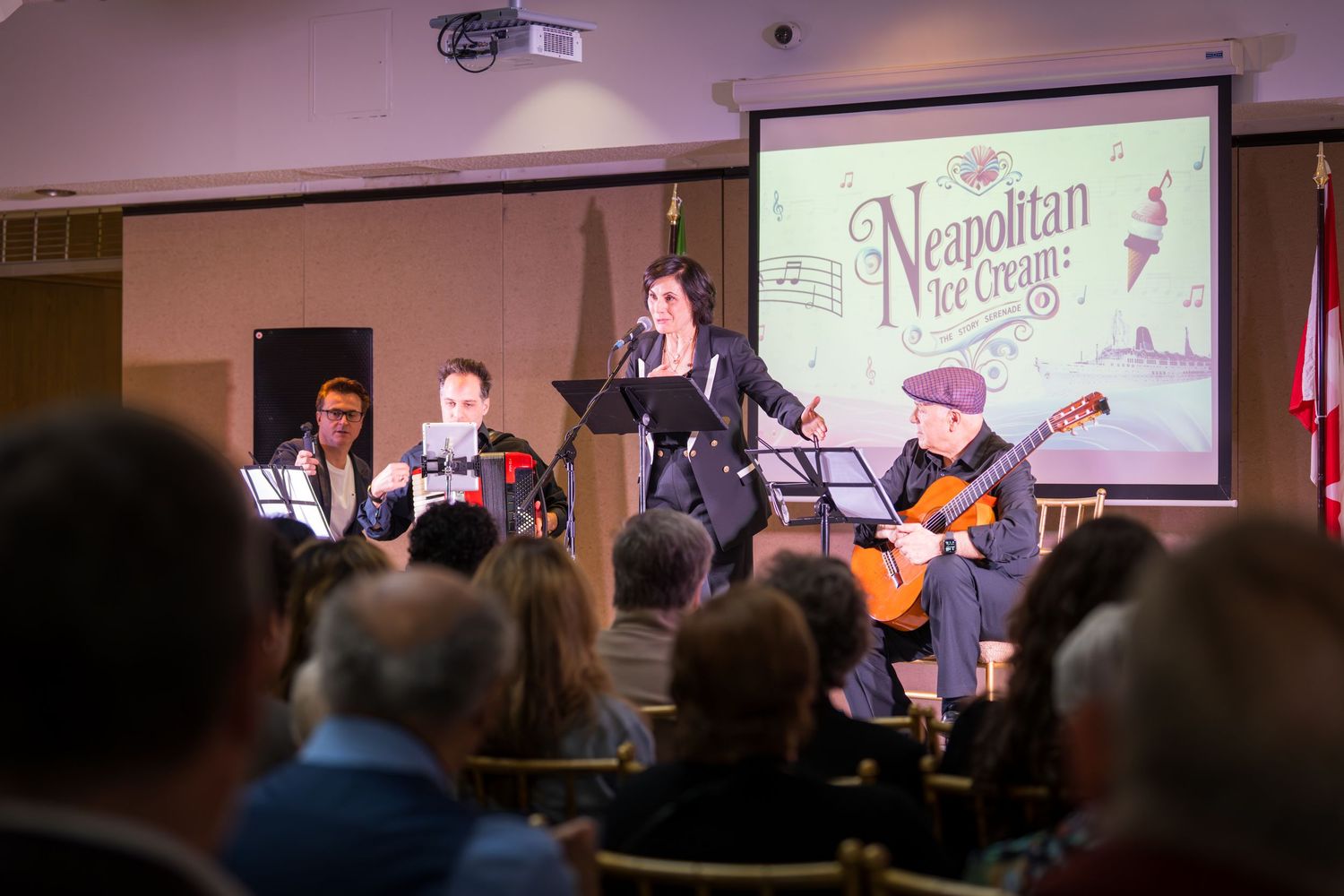 Live musical performance at Neapolitan Ice Cream themed event with singer and guitarist on stage before seated audience.