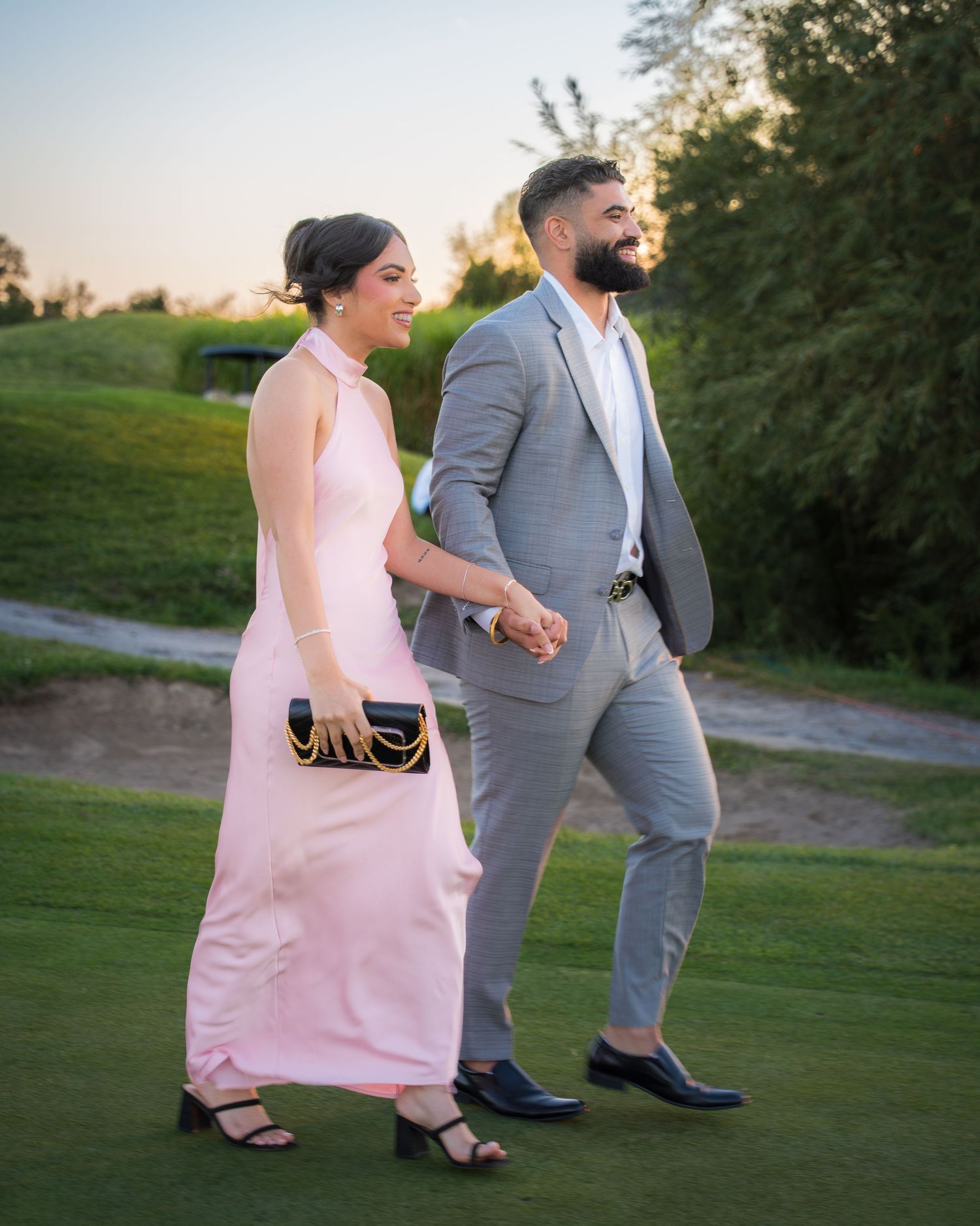 Couple strolling on landscaped path wearing pink dress and grey suit.