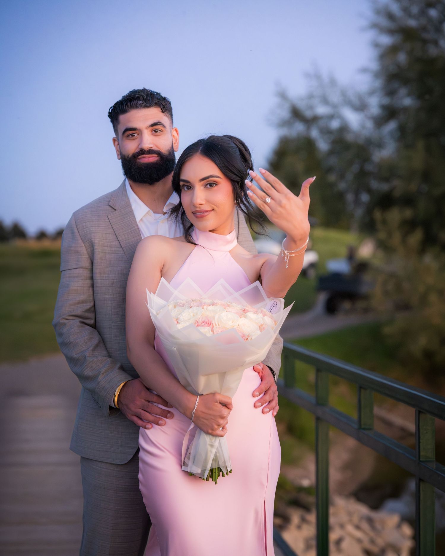 A couple poses with a white bouquet during their outdoor photoshoot at dusk.