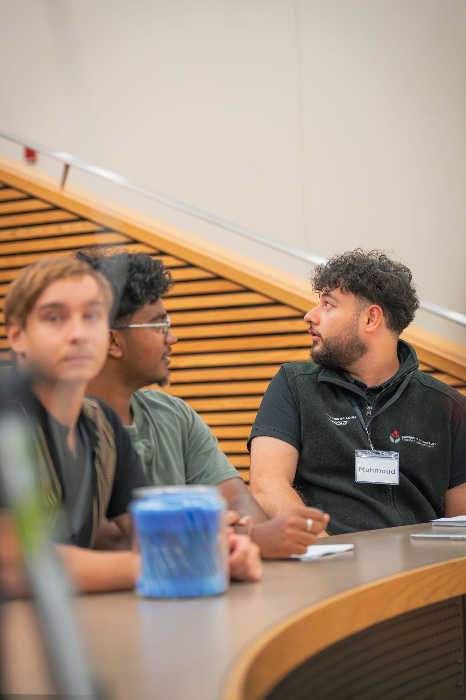 Students sitting in curved rows of a lecture hall during class discussion.