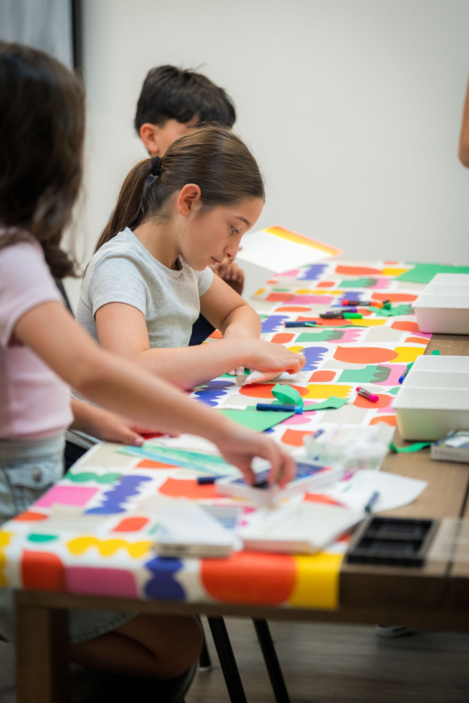 Children engage in a colorful paper craft activity at a table covered with vibrant cut-out shapes.