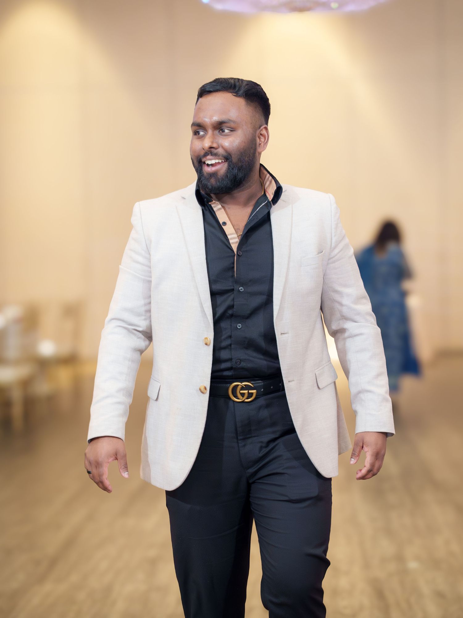 Groom in white blazer and black shirt poses in elegant indoor setting.