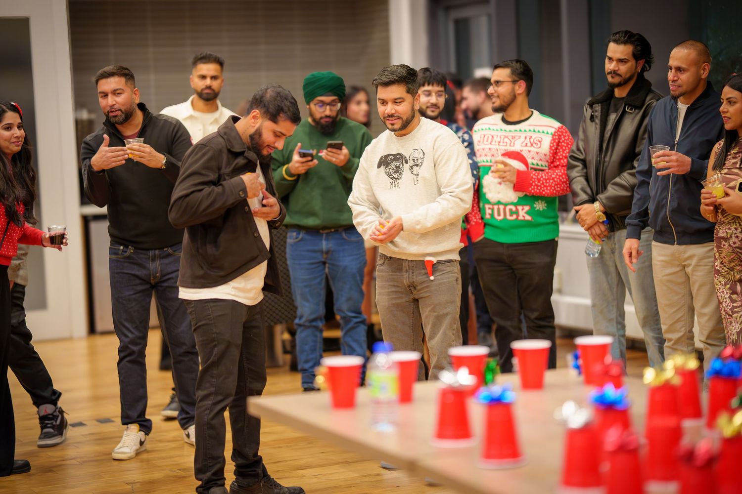 Crowd of people gathered around watching an indoor party game with red cups.