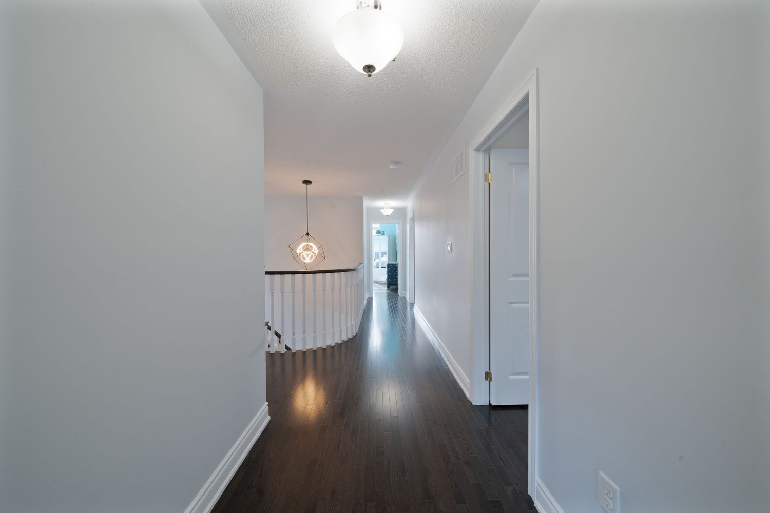 Modern interior hallway with pendant lights and white walls leading to a bright living space.