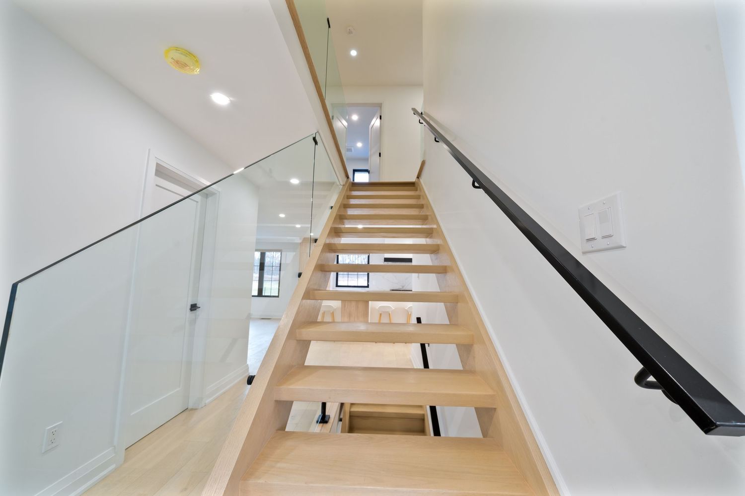 Modern white staircase with wooden steps and black handrails ascending in a minimalist interior space.
