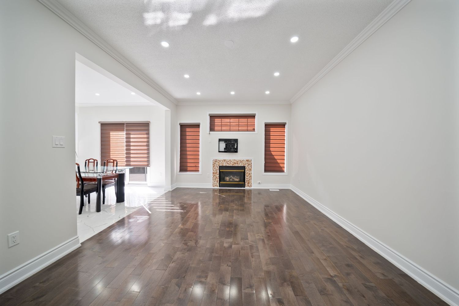 Long empty hallway with dark hardwood flooring, white walls, and ceiling spotlights.