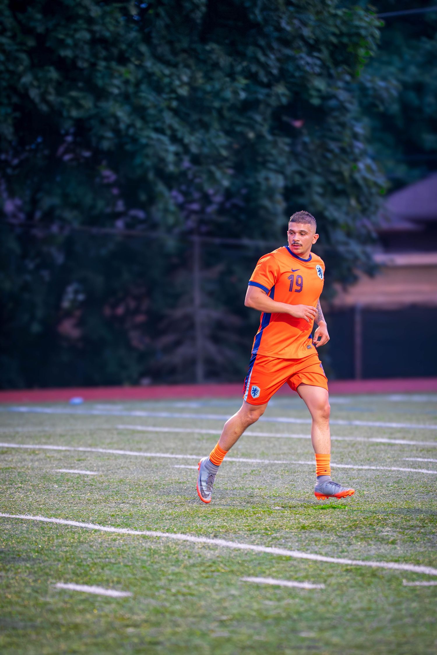 Soccer player in orange jersey moves across field during evening match.