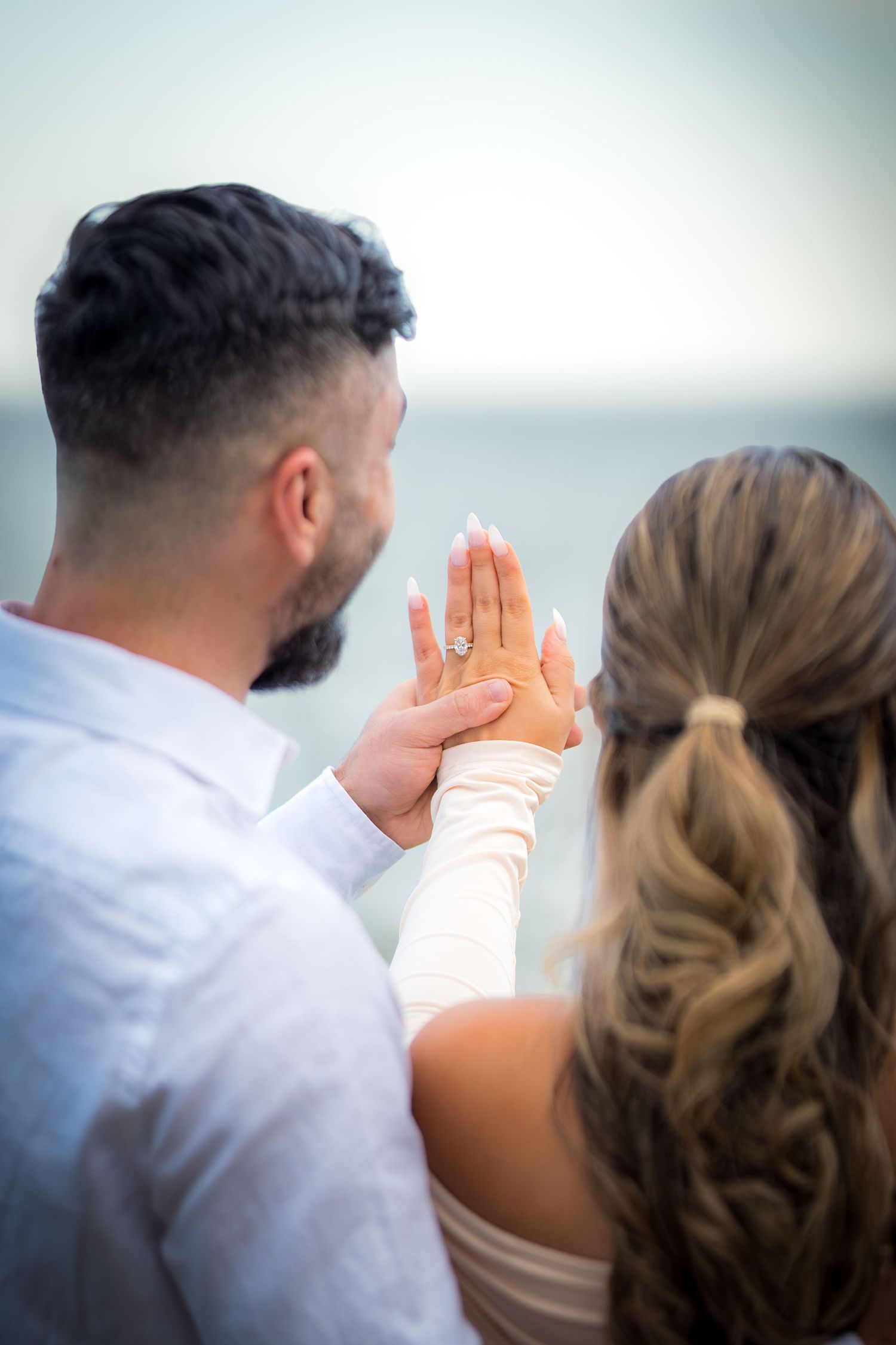 Couple in formal attire sharing an intimate moment by the ocean during a sunset photo session.