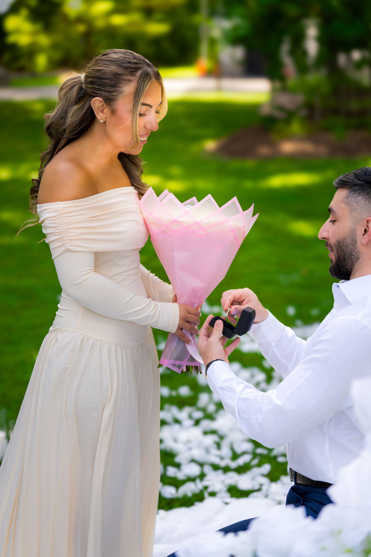 A surprise proposal moment captured in a garden with white petals scattered on the ground.