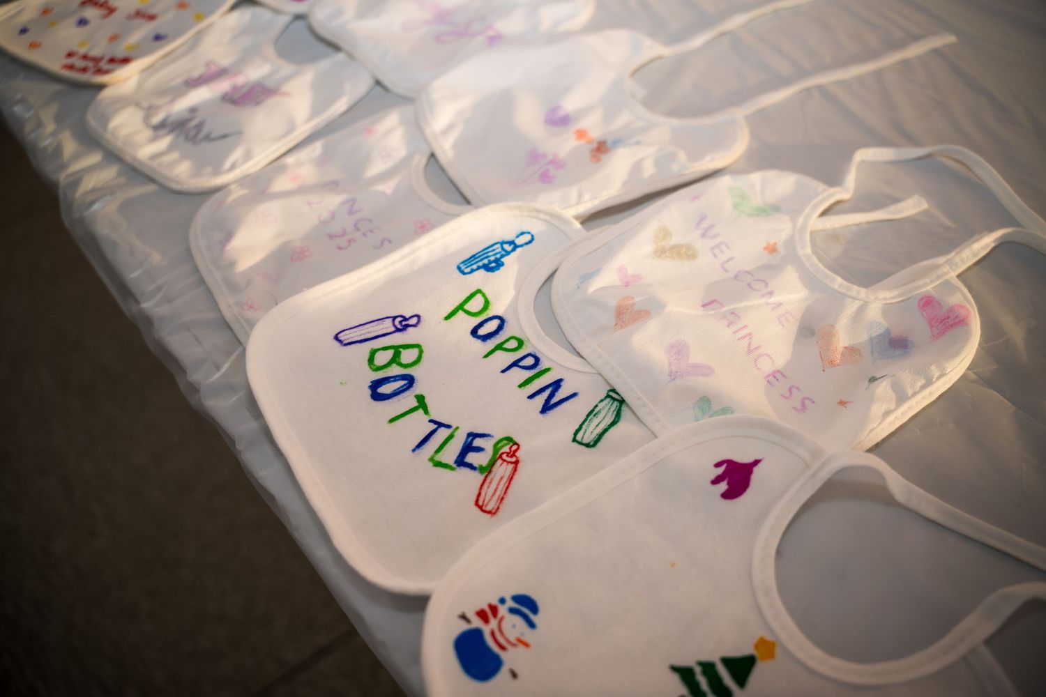 Collection of personalized baby bibs with colorful drawings laid out on floor.