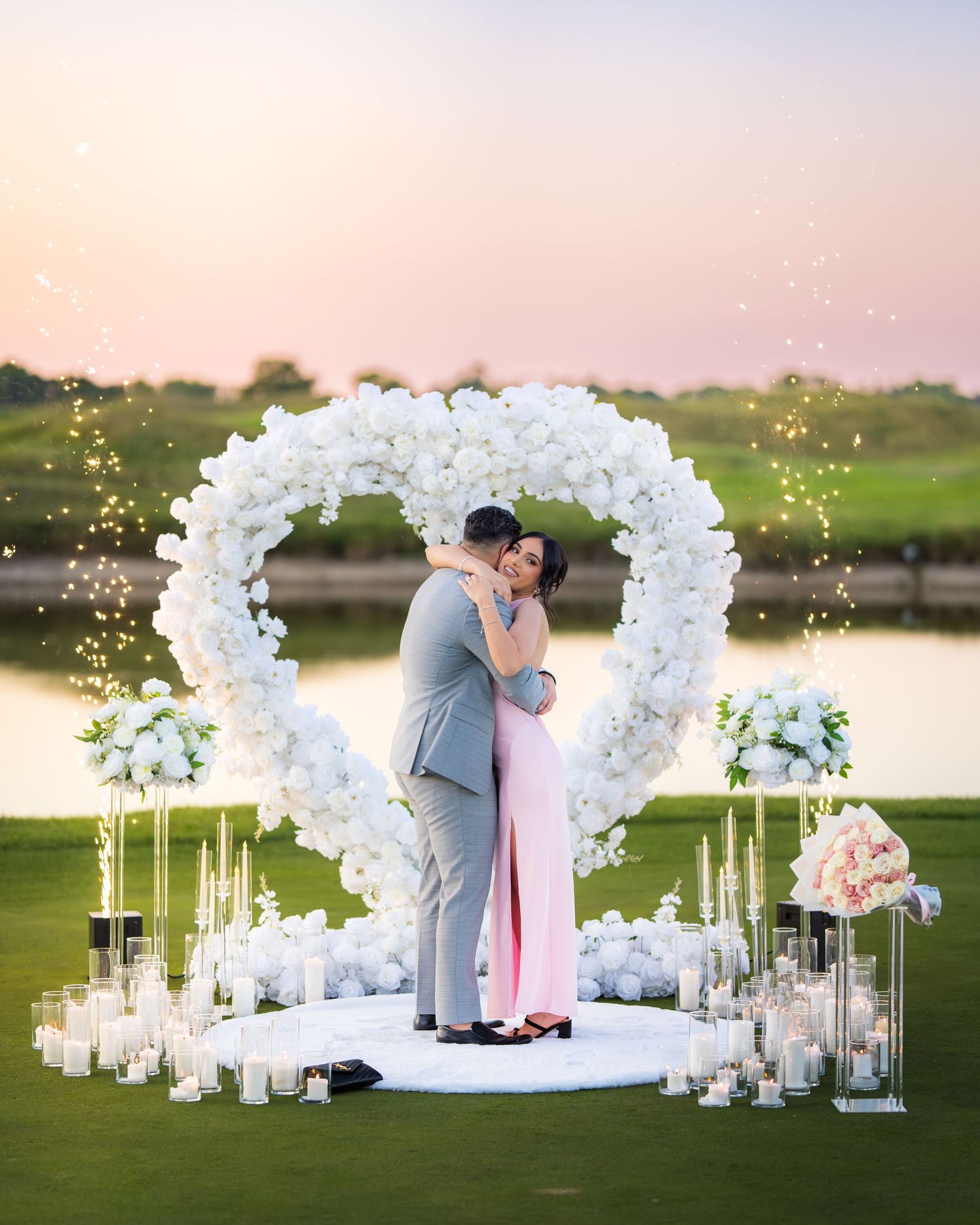 Elegant proposal setup with white floral arch and candlelit decorations by the water.