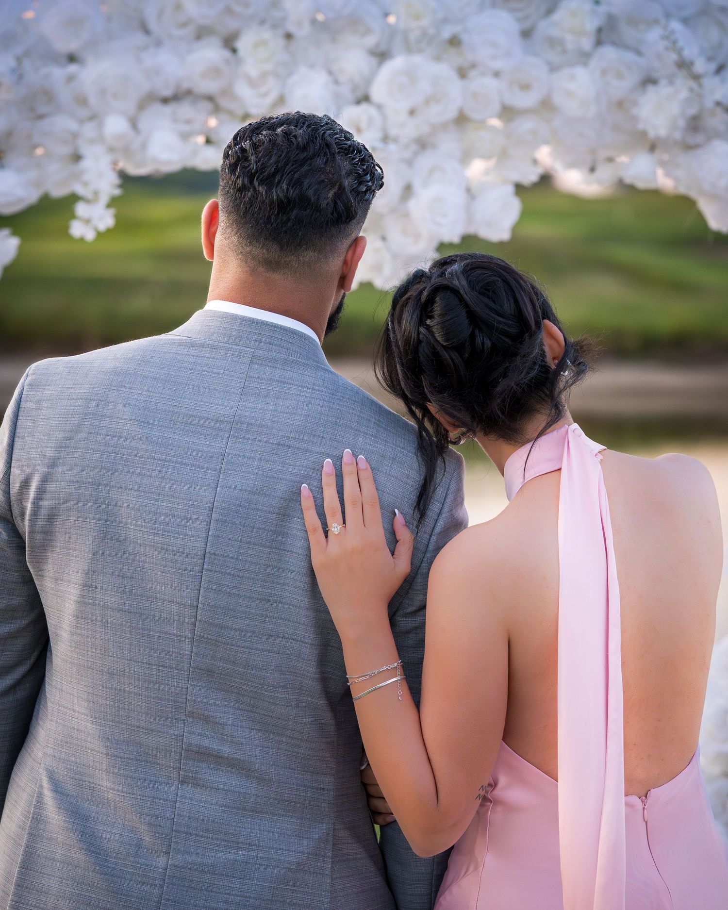 Close-up of couple in pink dress and grey suit standing by decorative arch.