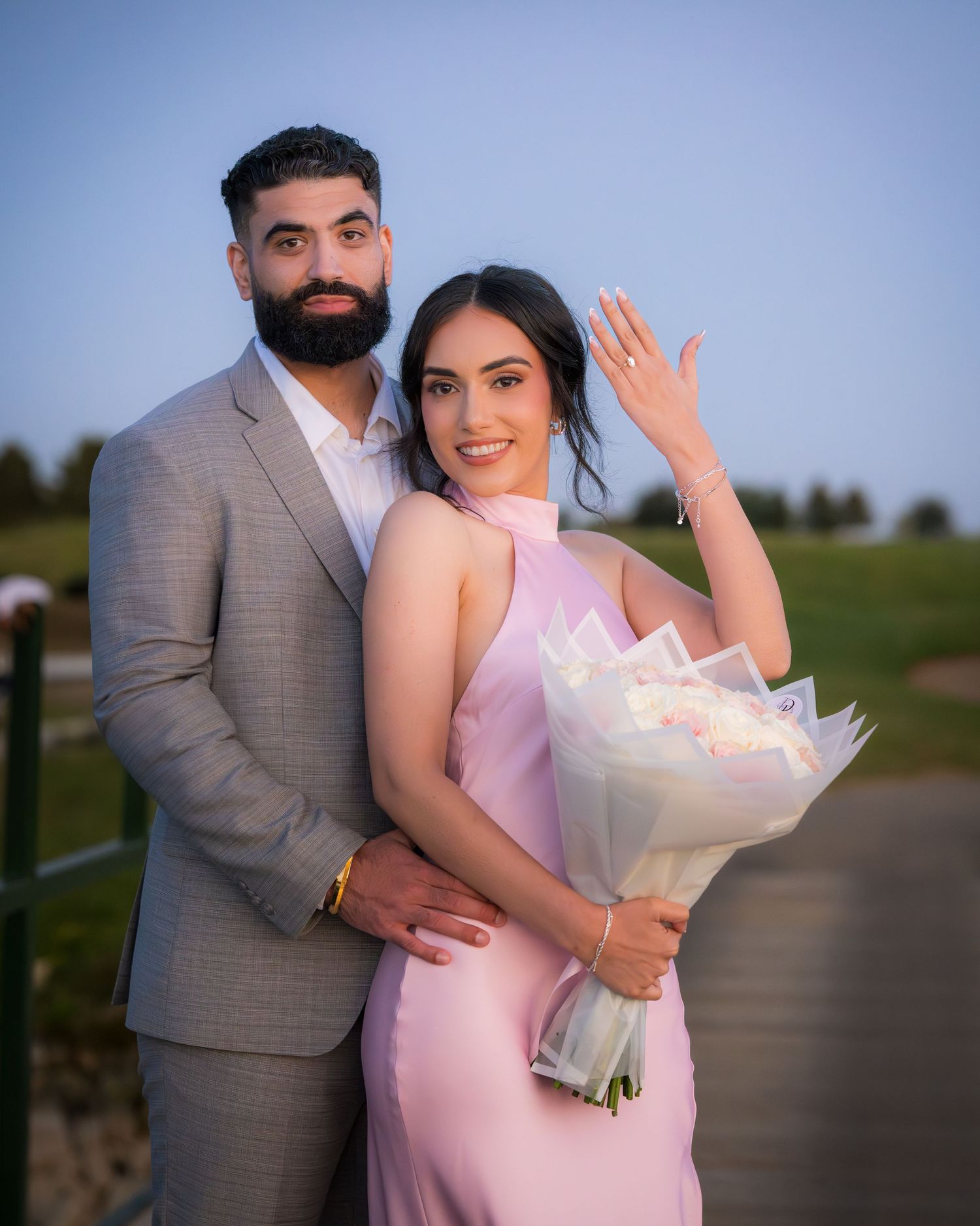 A romantic couple poses with a white flower bouquet during an outdoor photoshoot.