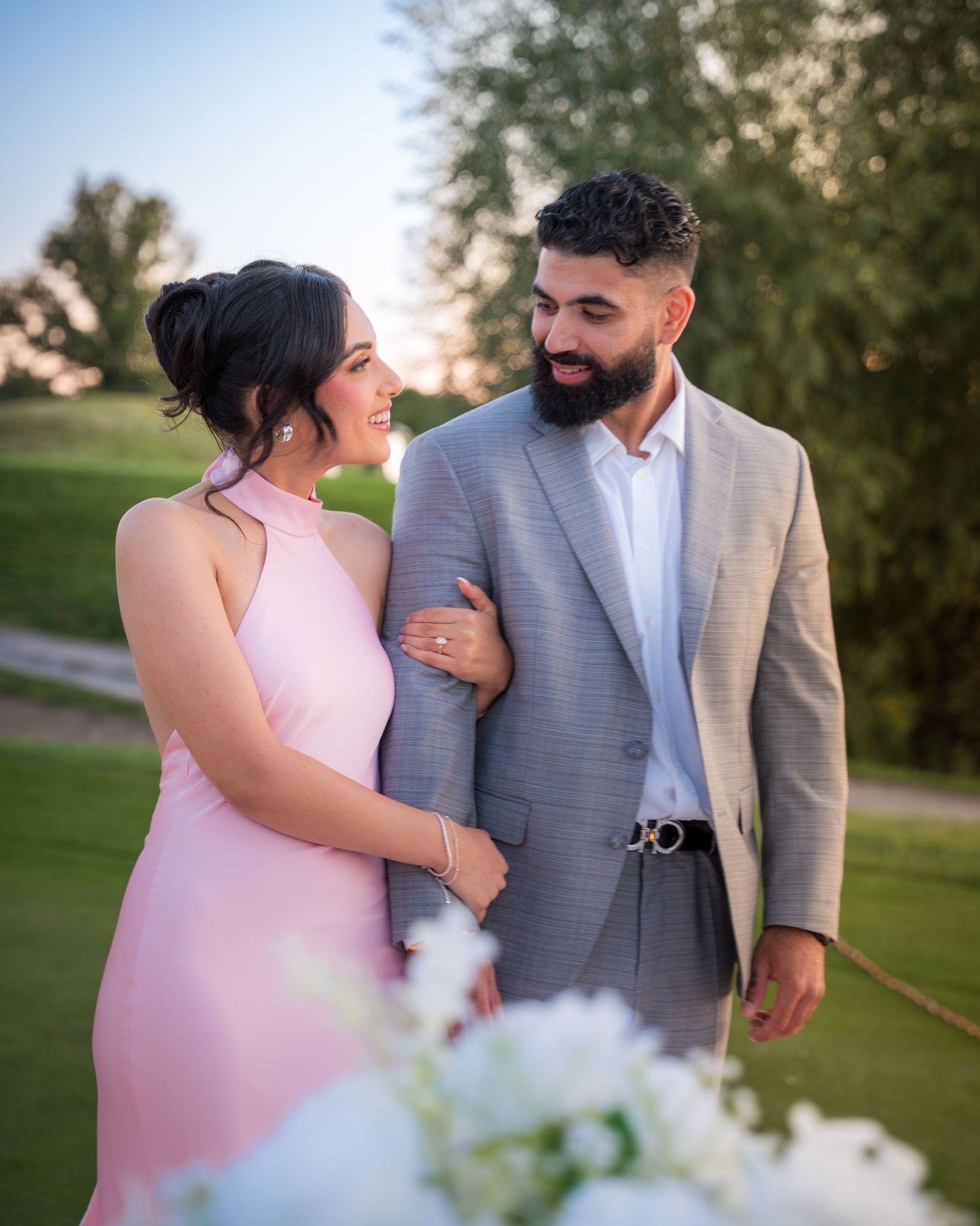 Intimate moment captured between a couple in formal attire on a golf course at dusk.