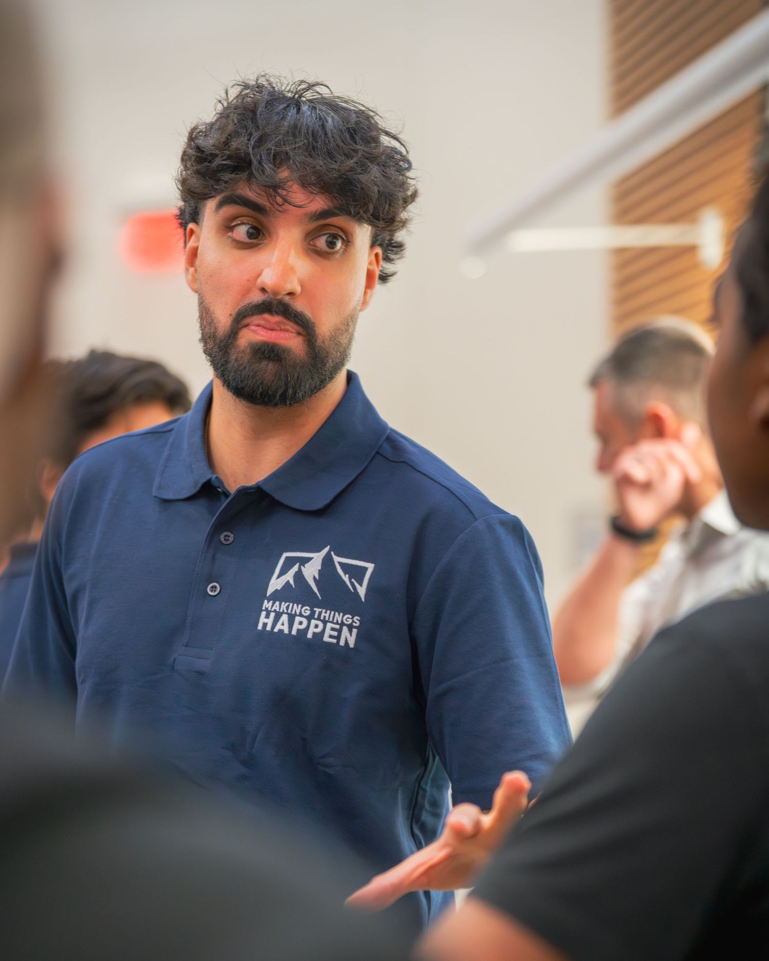 Staff member in navy polo with company logo engaging in discussion during event.