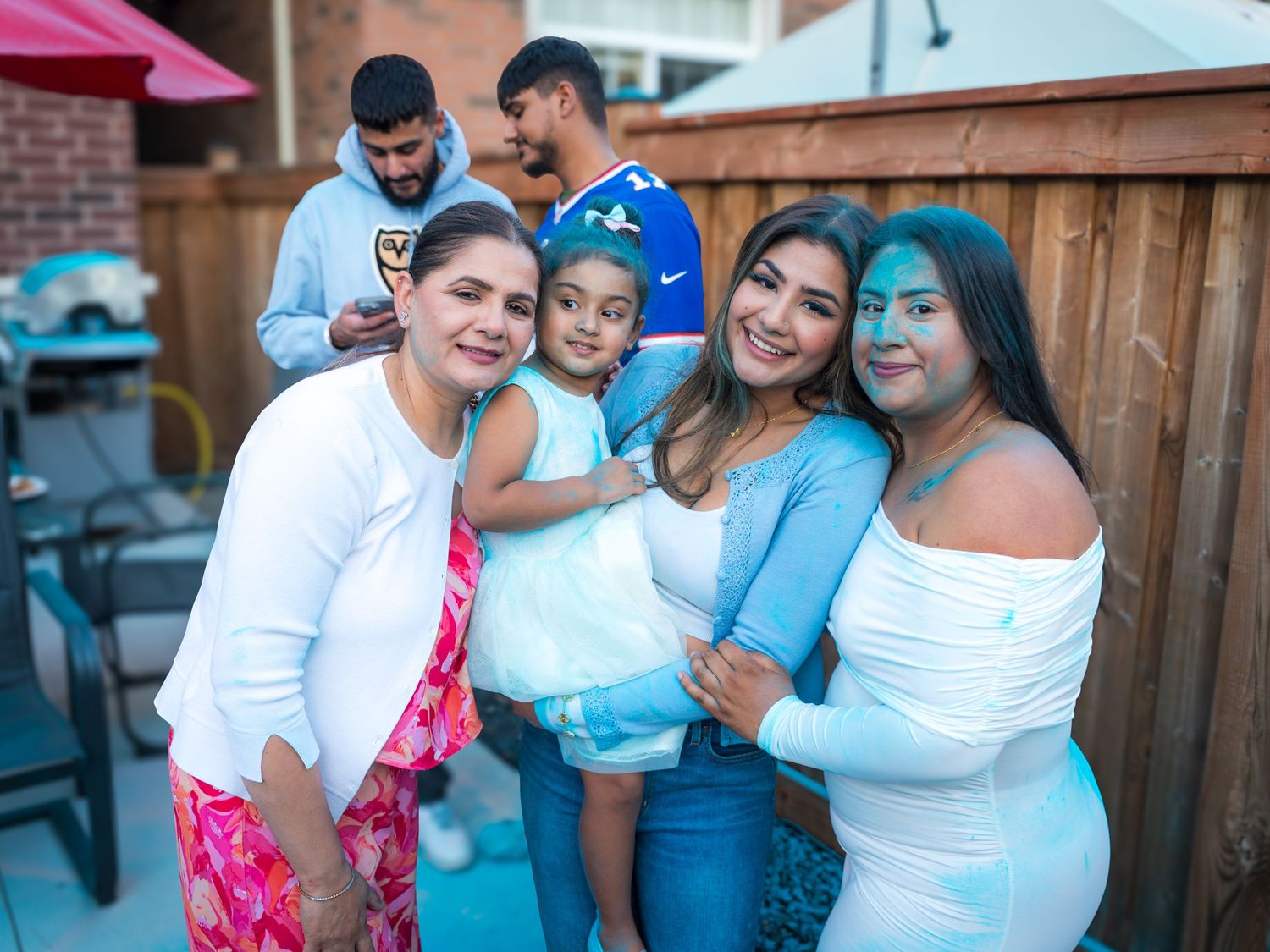 Four women and a child covered in blue powder celebrate a boy gender reveal outdoors.