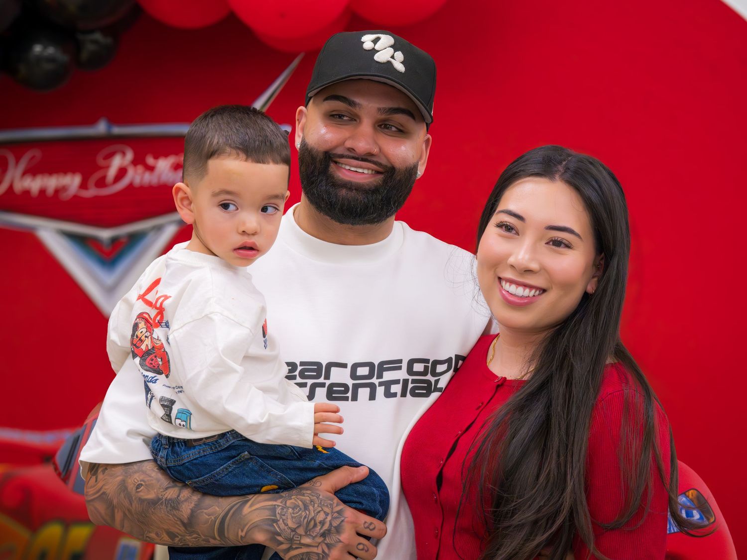 Family of three poses together at a Cars-themed birthday party with red balloon decorations.