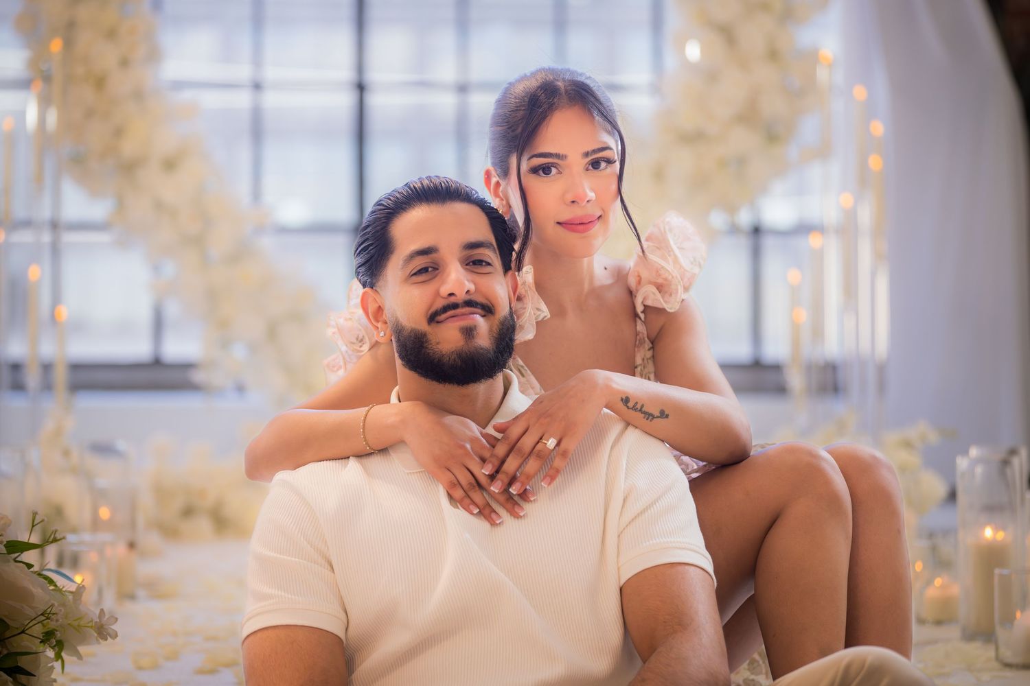 Couple sitting together smiling in front of elegant white floral arch decor.