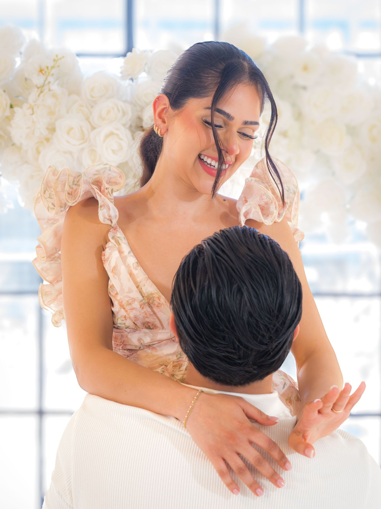 Happy woman embracing her fiance while laughing joyfully in a floral decorated venue.
