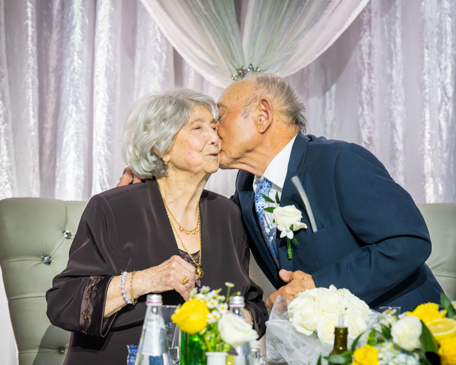 Elderly couple shares a tender kiss at their anniversary party celebration.