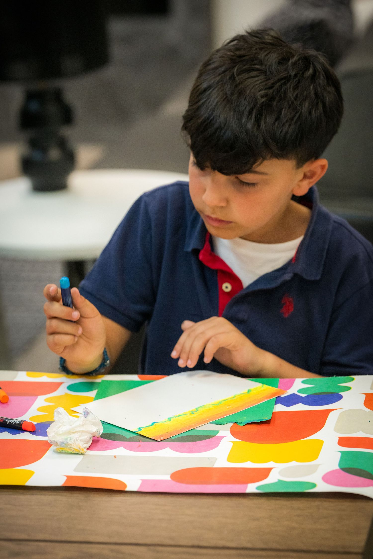 A focused young boy works on a colorful art project using markers and paper at a table.