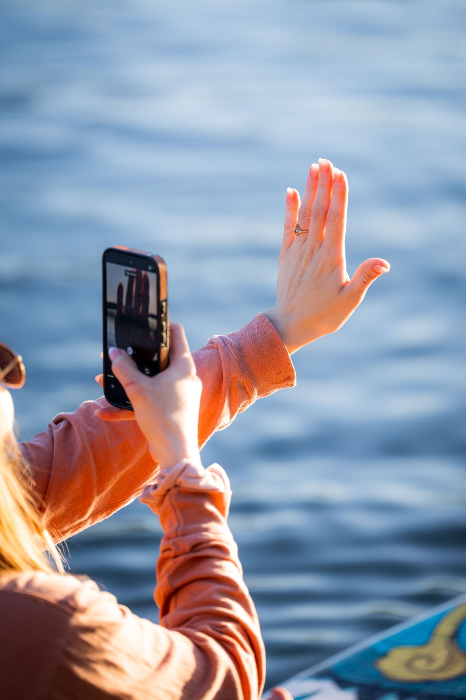 Woman photographing her engagement ring on a paddleboard on the water.