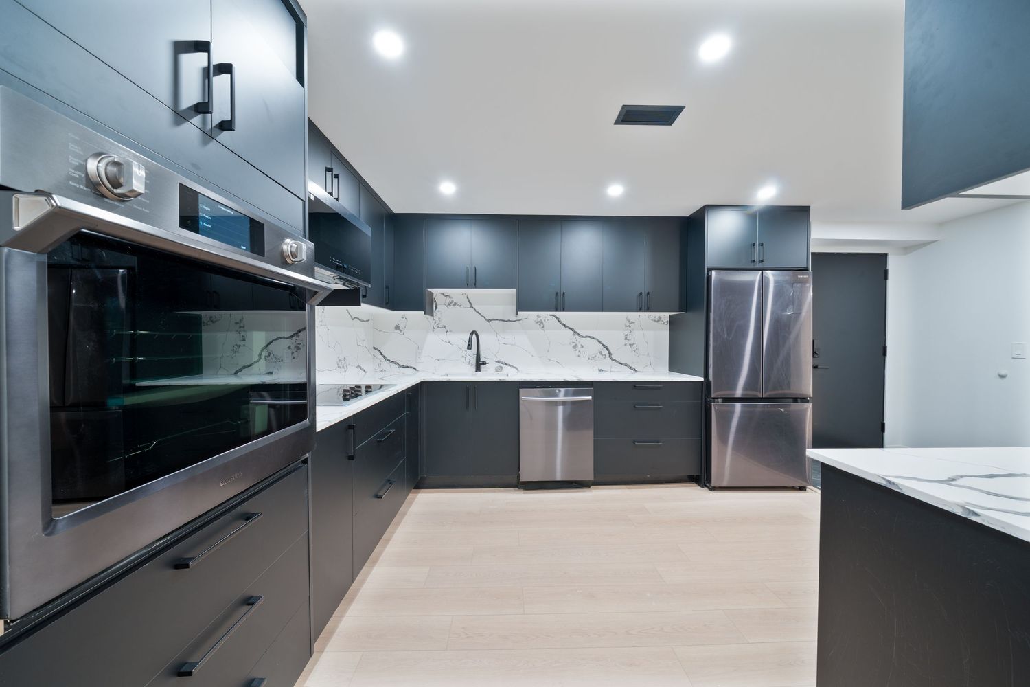 Modern kitchen interior with sleek dark cabinets, white countertops, and recessed lighting in a contemporary home.