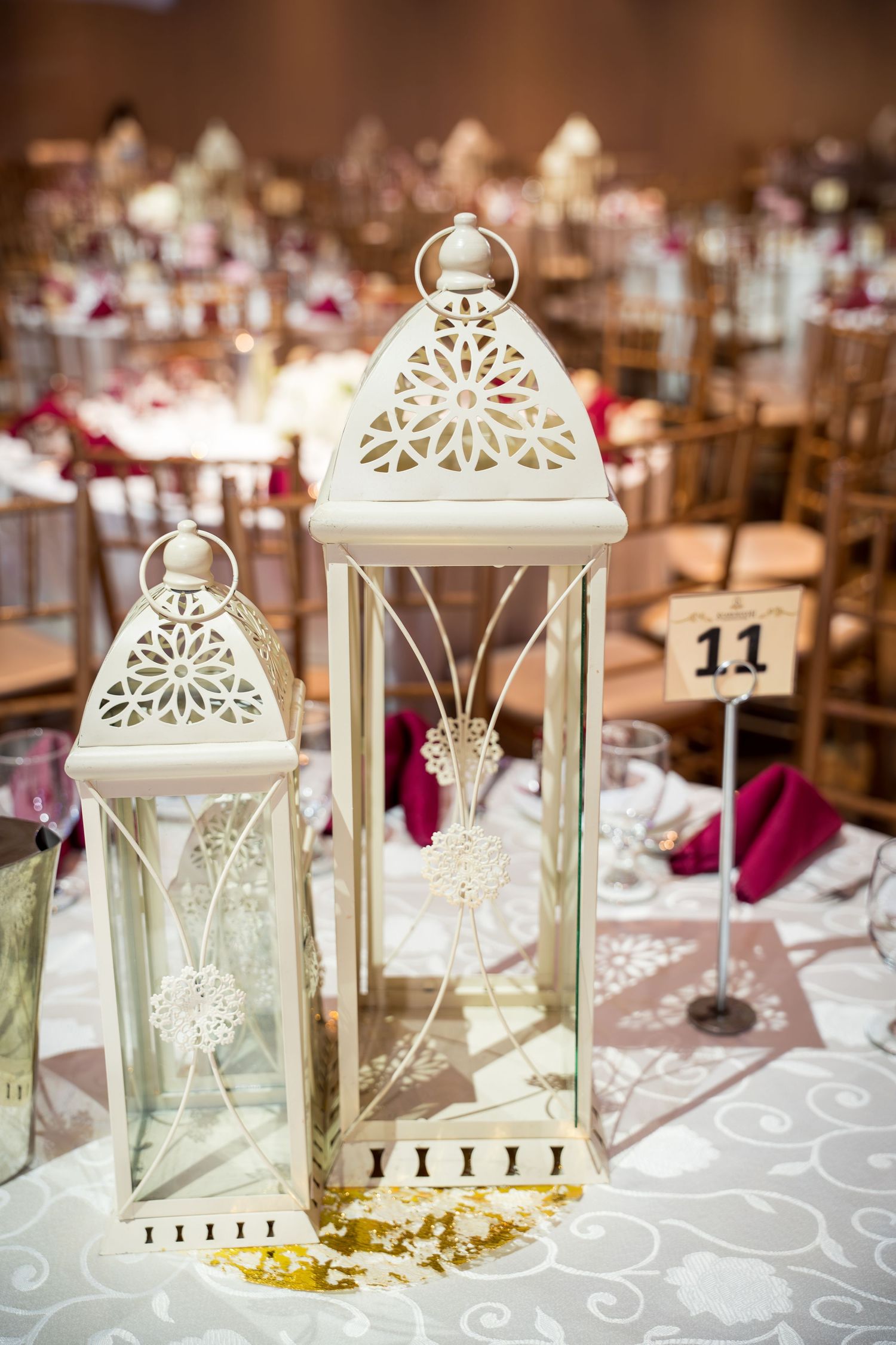 Elegant white lantern centerpieces with intricate cutout designs on reception tables with purple accents.