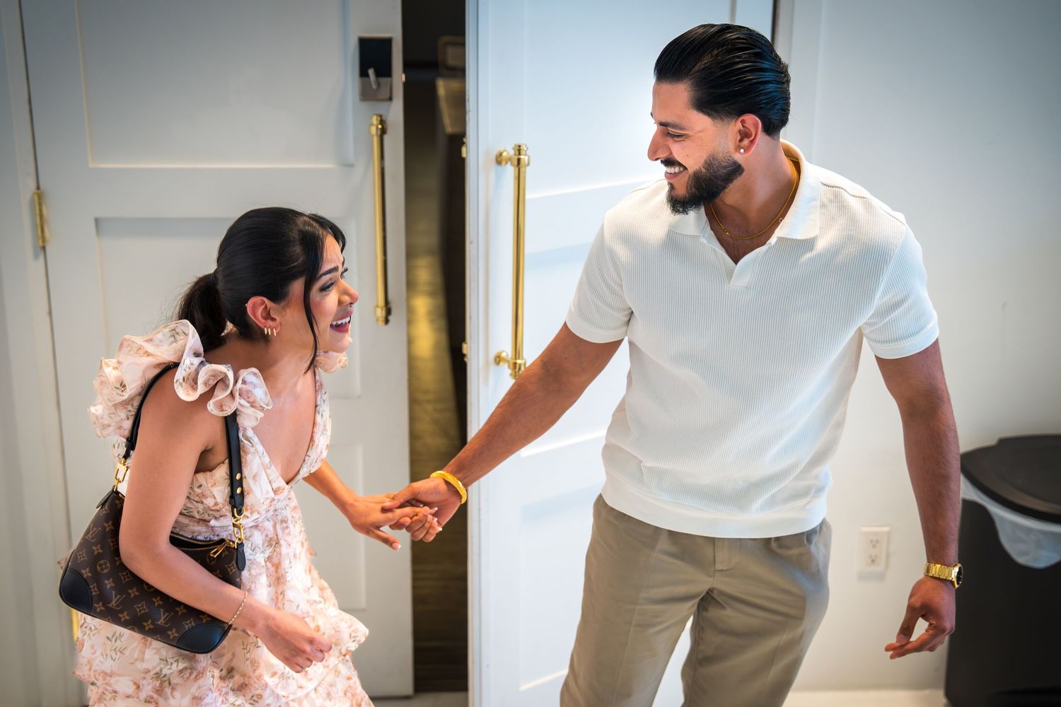 Man in white shirt shaking hands with woman in floral dress near gold bar.