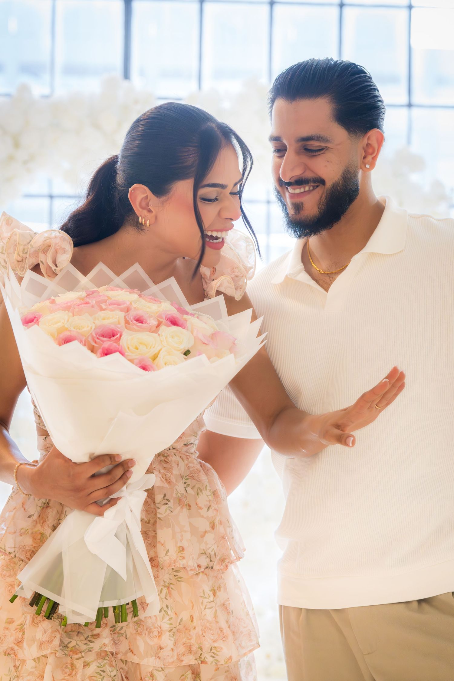 Happy couple sharing a joyful moment with a bouquet of pink and white roses.