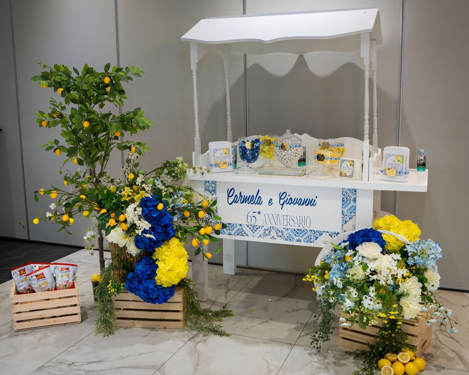 White decorative cart with blue tile design, yellow and blue flowers, lemon tree, and wooden crates for a wedding event.