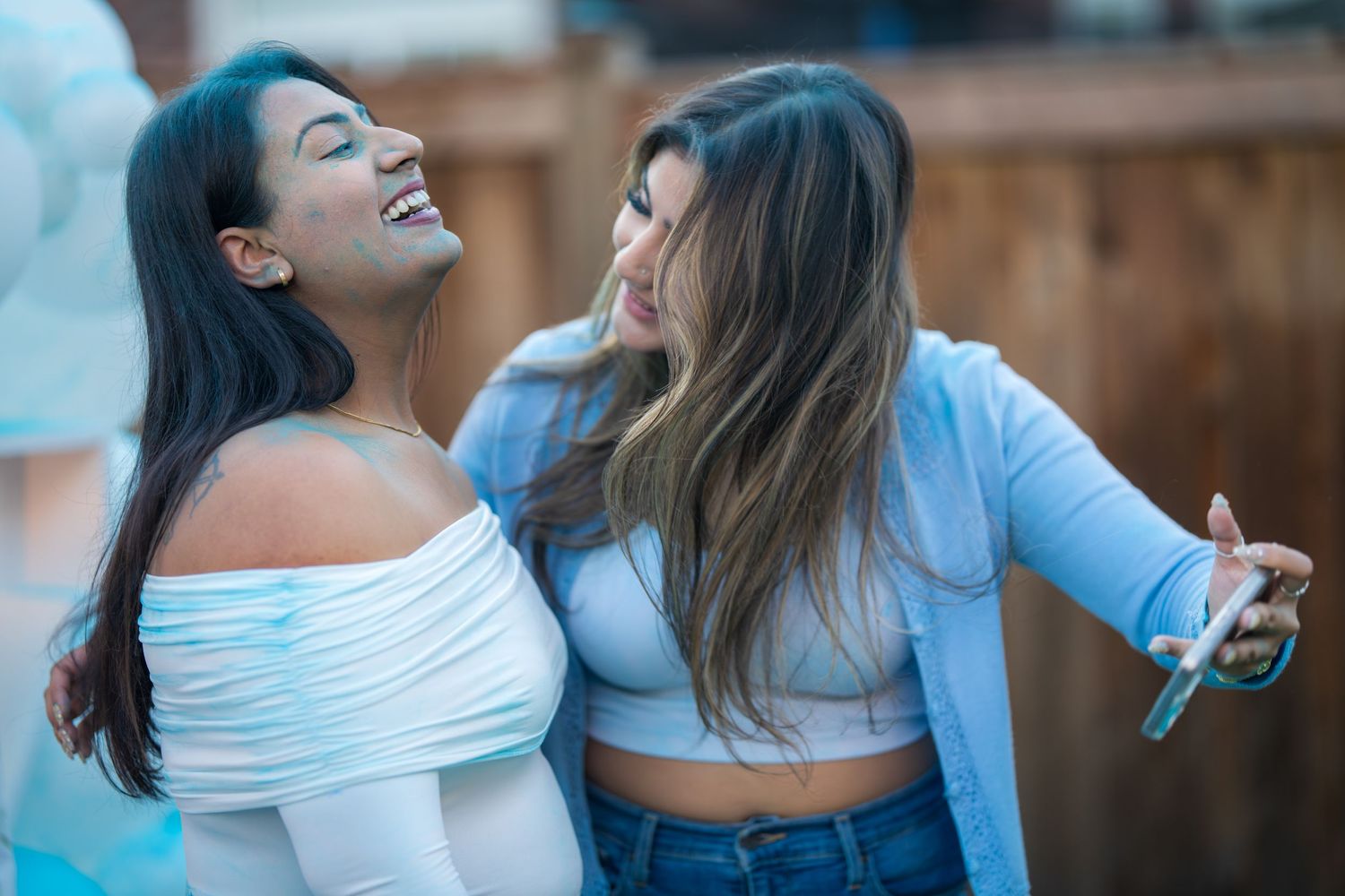 Two young women laughing and smiling together at an outdoor party celebration.